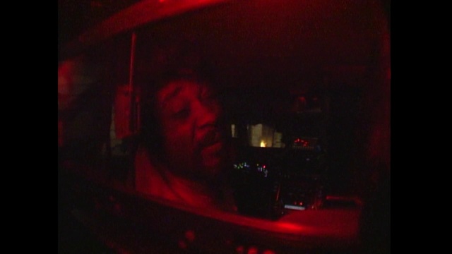 Video Reference: Red, Automotive lighting, Light, Lighting, Automotive tail & brake light, Auto part, Room, Darkness, Photography, Magenta, Indoor, Dark, Sitting, Lit, Front, Table, Man, Monitor, Holding, Laptop, Screen, Computer, Television, Standing, Sign, Human face, Person