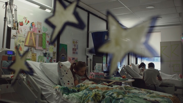 Video Reference: Ceiling, Room, Interior design, Visual arts, Art, World, Indoor, Bed, Sitting, Woman, Man, Table, Laying, Computer, Young, Bedroom, People, Holding, Group, Sleeping, Wall, Person, Human face, Clothing