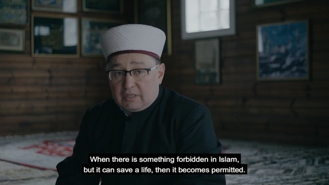 Video Reference: Headgear, Screenshot, Photo caption, Person, Indoor, Man, Holding, Sitting, Looking, Laptop, Table, Front, Using, Black, Young, Woman, Wearing, Computer, Cake, Large, Shirt, Room, Food, Plate, Remote, White, Standing, Hat, Text, Human face, Fashion accessory, Fedora, Clothing, Glasses