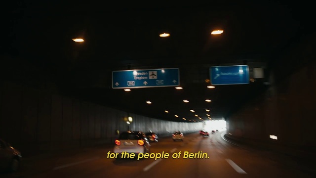 Video Reference: Night, Light, Road, Mode of transport, Street light, Automotive lighting, Lighting, Road trip, Lane, Infrastructure, Dark, Street, Television, Riding, Table, Man, Room, Large, Track, Sign, Plane, City, People, Air, Living, Traffic, Blurry, Standing, White, Screenshot, Text, Billboard, Highway