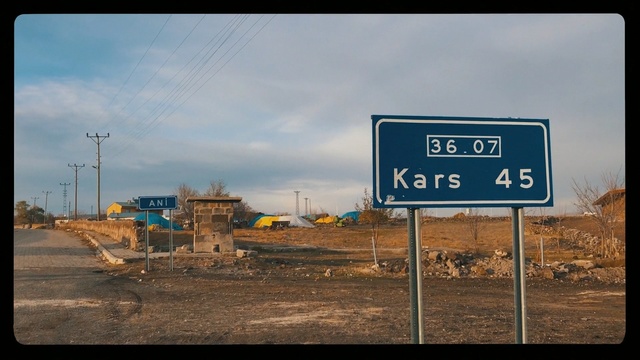 Video Reference: Traffic sign, Street sign, Signage, Sign, Road, Sky, Infrastructure, Landscape, Thoroughfare, Outdoor, Street, Sitting, Side, Pole, Highway, Intersection, Different, Blue, Traffic, White, Stop, Large, Cloudy, Yellow, Train, Dirt, City, Beach, Standing, Track, Text, Billboard, Cloud