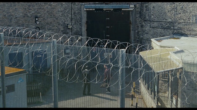 Video Reference: wire fencing, structure, wall, fence, chain link fencing, building, water, outdoor structure, metal, tree, Person