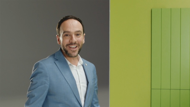 Video Reference: Yellow, White-collar worker, Suit, Businessperson, Smile, Business, Person, Man, Indoor, Standing, Front, Holding, Woman, Posing, Camera, Smiling, Green, Wearing, Mirror, Table, Sign, Door, Room, Young, Phone, Shirt, Computer, White, Wall, Human face, Clothing, Tie, Text, Headshot, Dress shirt