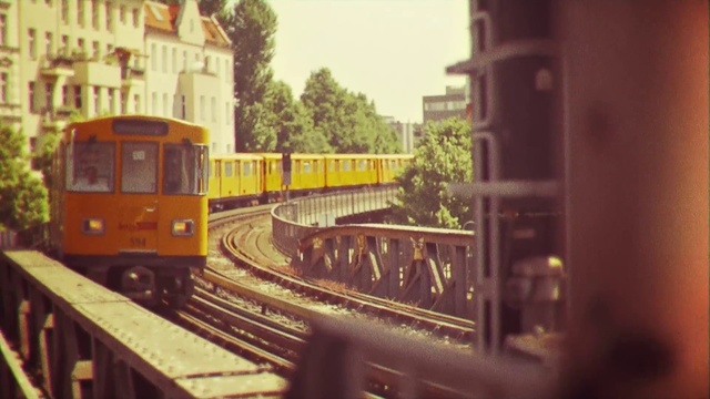 Video Reference: Transport, Mode of transport, Vehicle, Rolling stock, Railway, Train, Public transport, Track, Scale model, Railroad car, Outdoor, Building, Orange, Small, Sitting, Traveling, Bus, Platform, Street, Yellow, City, Side, Driving, Wooden, Old, Red, Parked, White, Station, Snow, Sign, Land vehicle, Railroad, Tree