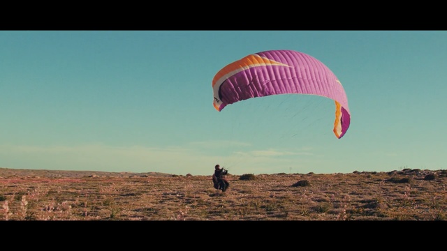 Video Reference: paragliding, air sports, sky, parachute, parachuting, windsports, cloud, daytime, horizon, field, Person