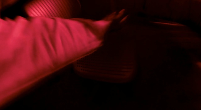 Video Reference: Red, Black, Light, Darkness, Orange, Pink, Brown, Finger, Maroon, Purple, Indoor, Person, Sitting, Table, Laptop, Dark, Man, Room, Looking, Front, Bed, Lit, Computer, Shirt, Wearing, White, Woman, Standing, Young, Blurry, Laying, Night