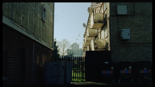 Video Reference: Urban area, Street, Architecture, Alley, Light, Snapshot, Town, Road, Sky, Infrastructure, Outdoor, Building, Brick, Sitting, Sidewalk, City, Large, Side, Standing, Red, Tall, Walking, Parked, Bus, Stop, Traffic, Man, Woman, Tower, White, Sign, Riding, Window, House, Text