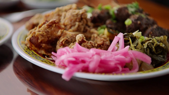 Video Reference: Dish, Food, Cuisine, Ingredient, Fried food, Produce, Cochinita pibil, Meat, Vegetarian food, Pakora, Plate, Table, Indoor, Sitting, Filled, Cake, Different, Close, Brown, Black, Salad, White, Bowl, Wooden, Holding, Fast food, Several