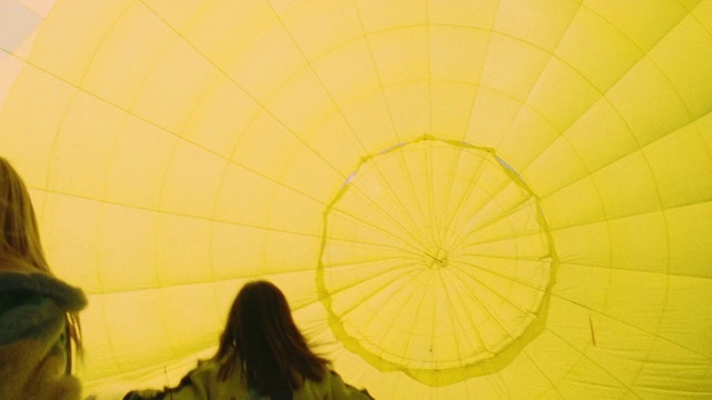 Video Reference: Yellow, Hot air balloon, Sky, Fun, Plant, Photography, Sunlight, Balloon, Vehicle, Leisure, Person, Indoor, Woman, Standing, Holding, Looking, Front, Umbrella, Young, Girl, Man, Mirror, Room, People, Phone, Playing, Laying, White