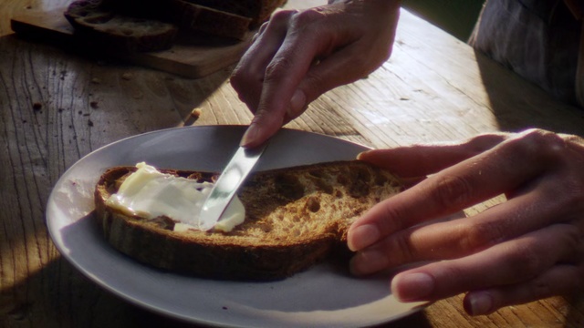 Video Reference: Food, Dish, Cuisine, Ingredient, Baked goods, Dessert, Recipe, Produce, Comfort food, Person, Table, Indoor, Cutting, Plate, Wooden, Man, Piece, Holding, Hand, Using, Sitting, Sandwich, Board, Cut, Knife, White, Cake, Fast food, Snack, Chocolate, Bread, Coffee, Dairy, Cooking, Snack food