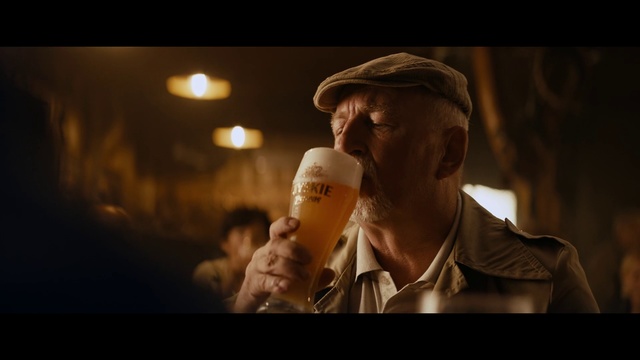 Video Reference: Alcohol, Human, Fun, Drink, Photography, Backlighting, Flash photography, Facial hair, Drinking, Darkness, Person, Man, Indoor, Looking, Holding, Wearing, Glasses, Sitting, Front, Standing, Food, Glass, Dark, Table, Shirt, Face, Hat, Room, Phone, Remote, Bottle, Human face, Soft drink, Beer, Hand