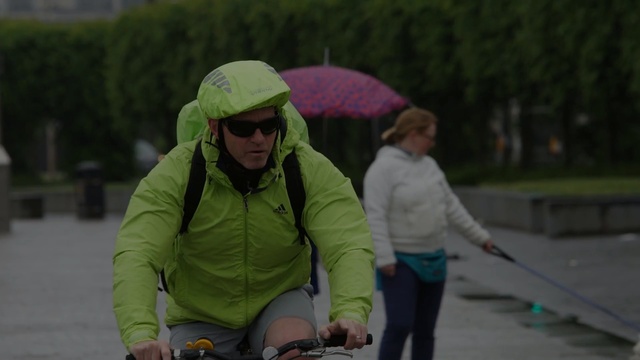 Video Reference: green, vertebrate, vehicle, headgear, personal protective equipment, recreation, fun, tree, car, cycling, Person