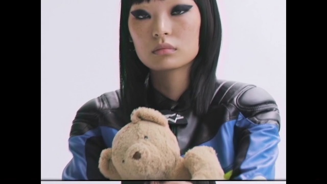 Video Reference: Face, Nose, Skin, Teddy bear, Head, Cheek, Beauty, Chin, Stuffed toy, Eye, Person, Teddy, Bear, Clothing, Stuffed, Indoor, Woman, Holding, Sitting, Looking, Wearing, Young, Small, Brown, Black, Table, Shirt, Girl, Screen, Laptop, Large, Standing, White, Room, Bed, Blue, Toy, Human face, Doll