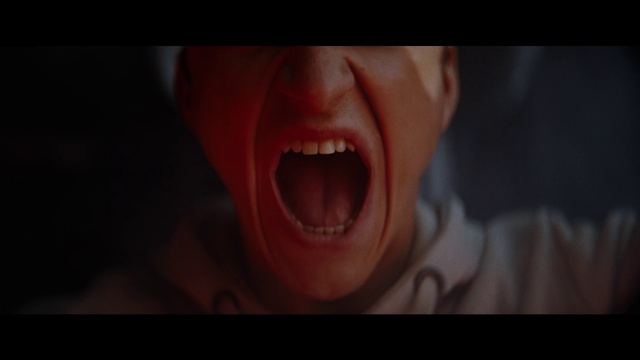 Video Reference: Tooth, Facial expression, Shout, Mouth, Fiction, Nose, Organ, Close-up, Tongue, Lip, Person, Indoor, Man, Holding, Looking, Dark, Close, Front, Black, Sitting, Red, Shirt, Face, Hand, Teeth, Food, Smiling, Orange, Screen, Wearing, Young, White, Glasses, Pink, Brushing, Eyes