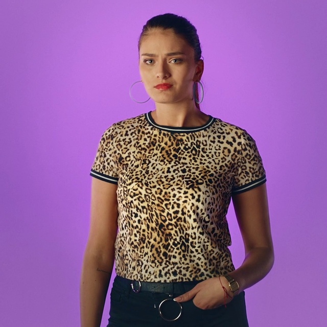 Video Reference: Clothing, Violet, Purple, Shoulder, Neck, Yellow, T-shirt, Fashion, Sleeve, Joint, Person, Indoor, Standing, Woman, Holding, Young, Looking, Dress, Front, Smiling, Girl, Green, Shirt, Wearing, Remote, Board, Phone, Room, Wall, Human face