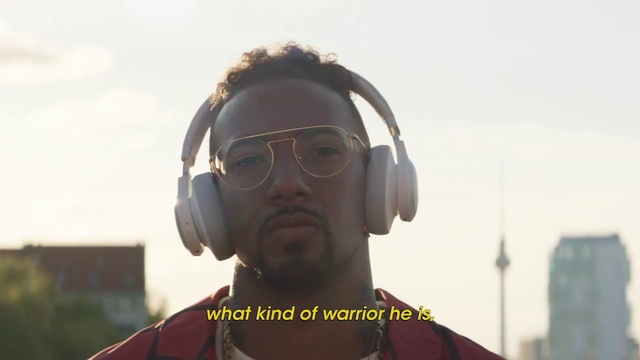 Video Reference: Headphones, Audio equipment, Personal protective equipment, Gadget, Technology, Eyewear, Glasses, Electronic device, Ear, Hearing, Outdoor, Person, Building, Man, Front, Holding, Looking, Wearing, Standing, Red, White, Yellow, Street, Large, Field, Sign, Water, Riding, Stop, Shirt, Hat, City, Traffic, Sky, Goggles, Human face, Screenshot, Spectacles