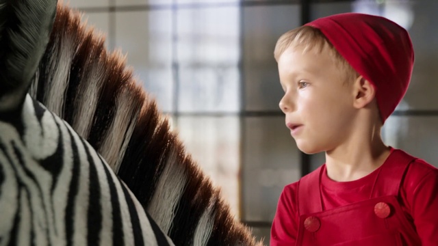 Video Reference: Hair, Child, Outerwear, Fur, Ear, Person, Indoor, Looking, Building, Young, Boy, Standing, Front, Hat, Man, Wearing, Holding, Little, Close, Woman, Head, White, Shirt, Turban, Red, Kitchen, Toddler, Baby, Human face