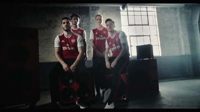 Video Reference: Social group, Fun, Photography, Font, Room, Screenshot, Performance, Sitting, Team, Art, Person, Man, Indoor, Holding, Red, Front, Standing, Young, Table, Black, Woman, Living, Playing, Remote, Clothing, Basketball, Sports uniform, Sports equipment, Text