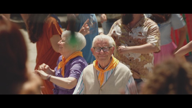 Video Reference: People, Community, Event, Fun, Adaptation, Crowd, Happy, Child, Glasses, Smile, Person, Indoor, Cake, Man, Woman, Looking, Photo, Table, Standing, Holding, Birthday, Food, Cutting, Glass, Group, Wedding, Screen, White, Cut, Display, Shirt, Video, Playing, Room, Human face, Text, Clothing