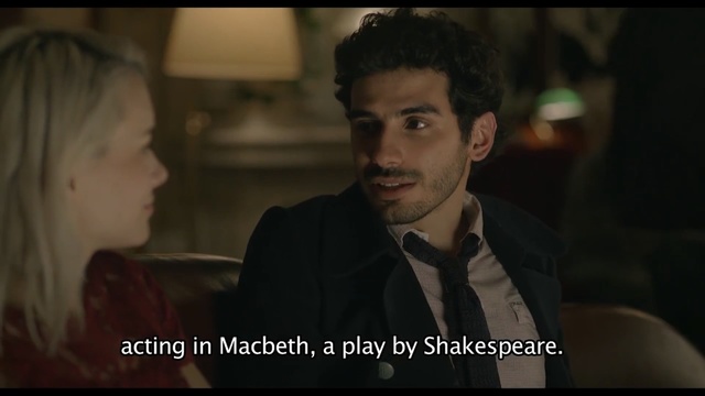 Video Reference: Human, Movie, Photo caption, Adaptation, Smile, Fun, Screenshot, Conversation, Scene, Gentleman, Person, Indoor, Man, Sitting, Looking, Front, Table, Suit, Photo, Young, Wearing, Camera, Holding, Smiling, Glasses, Food, Laptop, Woman, Standing, Computer, Black, Shirt, Room, Desk, White, People, Phone, Human face, Clothing, Text, Portrait