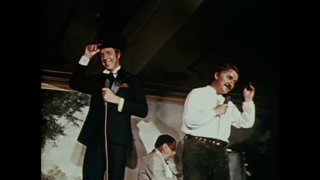 Video Reference: Photograph, Social group, Formal wear, Male, Fun, Suit, Event, Gentleman, Music, Performance, Person, Man, Standing, Posing, Wearing, Holding, Front, Woman, Black, Skiing, Talking, Dressed, Dark, Snow, People, Walking, Room, Night, Group, White, Sign, Phone, Suitcase, Riding, Slope, Street, Clothing, Concert