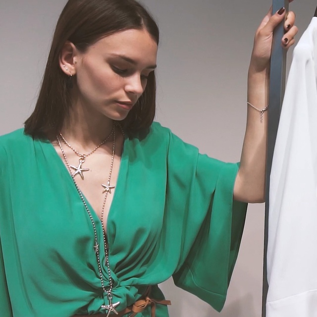 Video Reference: Green, Turquoise, Neck, Arm, Shoulder, Outerwear, Fashion accessory, Long hair, Jewellery, Necklace, Person, Woman, Clothing, Indoor, Looking, Shirt, Standing, Lady, Man, Cellphone, Dress, Holding, Wearing, Phone, Cake, Table, Talking, Young, People, Blue, White, Room, Wall, Human face, Fashion