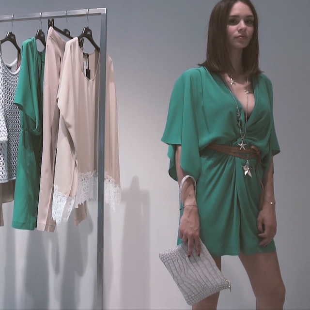 Video Reference: Clothing, Green, Clothes hanger, Dress, Day dress, Robe, Outerwear, Fashion design, Room, Sleeve, Person, Indoor, Woman, Standing, Wearing, Dressed, Man, Front, Holding, Young, Clothes, Walking, Shirt, White, Umbrella, Wall, Fashion, Coat, Handbag, Blouse, Skirt