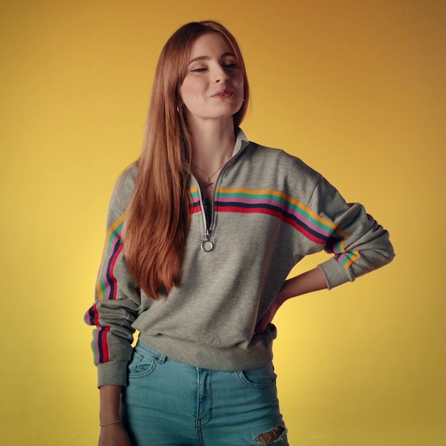 Video Reference: Clothing, Shoulder, Yellow, Sleeve, Waist, Jeans, Joint, Shirt, Outerwear, T-shirt, Person, Indoor, Standing, Holding, Man, Woman, Young, Living, Striped, Wearing, Room, Girl, Hand, Using, Playing, Video, Remote, Phone, Game, Wall, Smile, Human face, Fashion accessory, Trousers