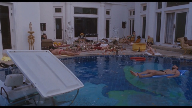 Video Reference: Swimming pool, Property, Leisure, Leisure centre, Building, Indoor, Table, Window, Counter, Food, Water, Sitting, Sink, Kitchen, Woman, Room, Plate, Man, Bowl, Vase, Large, Blue, White, Cake, Living, Standing, Holding, People, Group, Swimming, Pool, Cluttered