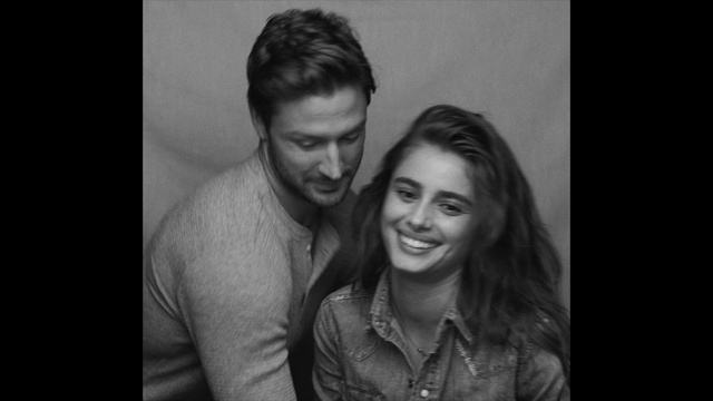 Video Reference: Hair, Photograph, People, Facial expression, Smile, Hairstyle, Black-and-white, Monochrome photography, Portrait, Forehead, Person, Indoor, Man, Front, Looking, Photo, Woman, Window, Standing, Table, Dark, Holding, Young, Sitting, Shirt, Laptop, Lit, Smiling, Computer, Black, White, Phone, Human face, Clothing, Black and white