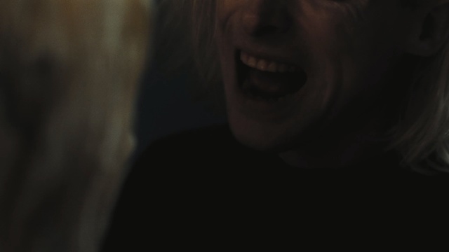 Video Reference: Face, Black, Facial expression, Nose, Head, Lip, Smile, Darkness, Mouth, Chin, Looking, Indoor, Person, Front, Camera, Standing, Smiling, Woman, Sitting, Holding, Close, Door, Room, Laptop, Man, Shirt, Computer, Red, White, Food, Dog, Human face, Portrait, Eyes, Selfie, Eyebrow, Jaw, Cheek, Staring, Blur