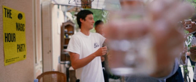 Video Reference: Arm, Person, Indoor, Table, Man, Food, Standing, Kitchen, Meal, Woman, Holding, Restaurant, Young, Wine, Front, Shirt, Pizza, Counter, Sitting, Glasses, Boy, People, Eating, Plate, Cooking, White, Human face, Clothing