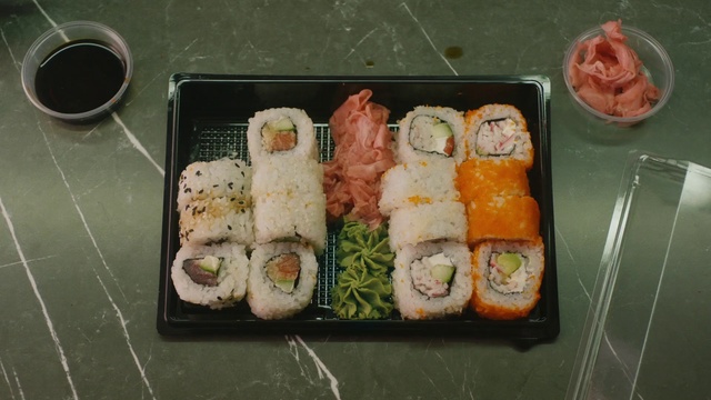 Video Reference: Dish, Food, Cuisine, Gimbap, Sushi, California roll, Steamed rice, Ingredient, Meal, Rice ball, Person, Container, Box, Sitting, Small, Tray, Table, Plastic, Bunch, Filled, Different, Plate, Group, Seafood, Fast food, Delicacy, Sakana, Ekiben, Japanese cuisine, Salmon, Garnish, Nori, Okazu, Sashimi, Several