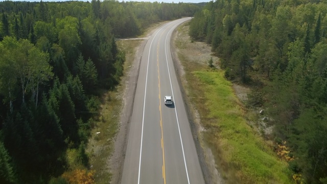 Video Reference: Road, Highway, Thoroughfare, Lane, Asphalt, Infrastructure, Freeway, Road surface, Shoulder, Mode of transport, Person, Scene, Grass, Train, Outdoor, Track, Traveling, Forest, Coming, Country, Wooded, Long, Driving, Side, Surrounded, Green, Narrow, Railroad, Mountain, Field, Riding, Tall, Tree, Way, Vehicle, Tarmac, Car, Tar, Land vehicle, Wood, Lush