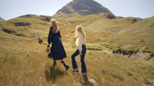 Video Reference: People in nature, Photograph, Highland, Mountainous landforms, Hill, Grassland, Natural landscape, Fell, Ecoregion, Wilderness, Grass, Outdoor, Mountain, Nature, Field, Standing, Green, Walking, Brown, Young, Woman, Grassy, Wearing, Girl, Rock, Man, White, Sky, Clothing, Person, Hiking, Footwear, Hillside