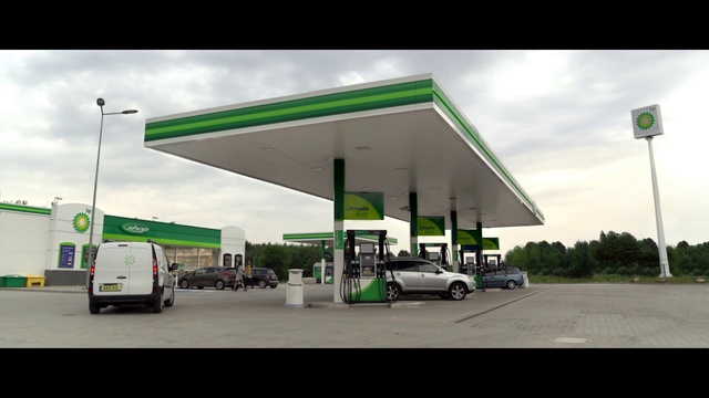 Video Reference: Filling station, Gasoline, Fuel, Building, Petroleum, Vehicle, Business, Shade, Car, Gas, Outdoor, Road, Green, Sign, Street, Parked, Runway, Tarmac, Truck, Man, Airplane, Sitting, Plane, Standing, Woman, Large, White, Station, Cloudy, Jet, Driving, People, Traffic, Riding, City, Bus, Air, Group, Sky, Text, Land vehicle, Wheel, Day, Highway