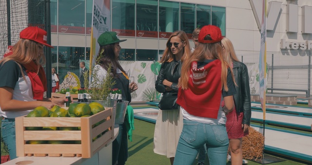 Video Reference: Green, Community, Youth, Organism, Headgear, Event, Plant, Recreation, Tourism, Leisure, Person, Woman, Building, Standing, Girl, Table, Front, Food, People, Holding, Young, Group, Man, Phone, Kitchen, Walking, Bench, Street, Store, Umbrella, Room, Train, Clothing, Smile, Human face, Fashion accessory, Hat, Sunglasses, Glasses