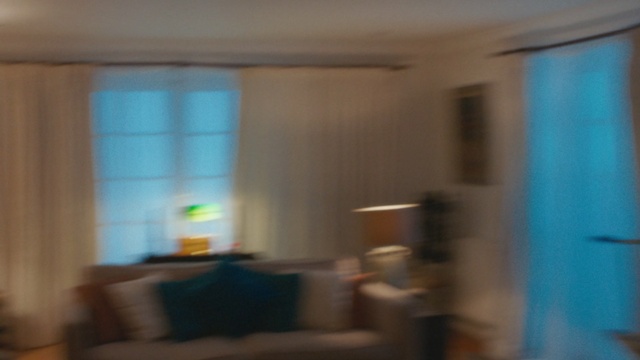 Video Reference: Room, Property, Ceiling, House, Wall, Living room, Interior design, Floor, Window covering, Home, Person, Indoor, Window, Kitchen, Table, Living, Small, Large, Woman, Television, Sitting, White, Counter, Glass, Door, Wooden, Standing, Blue, Holding, Stove, Sink, Blurry, Man, Refrigerator, Bed, Furniture, Blur