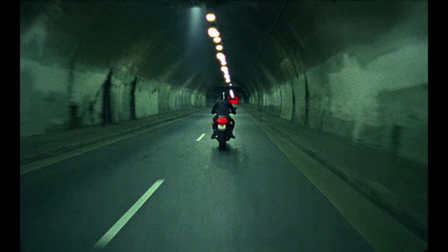 Video Reference: Road, Lane, Tunnel, Mode of transport, Atmospheric phenomenon, Infrastructure, Highway, Asphalt, Thoroughfare, Darkness, Outdoor, Light, Street, Scene, Dark, Traffic, Red, Blurry, View, Sunset, Sitting, Rain, Stop, Side, Driving, Green, Riding, Sun, Night, City, Intersection, Motorcycle, Train, Way, Vehicle, Land vehicle, Text
