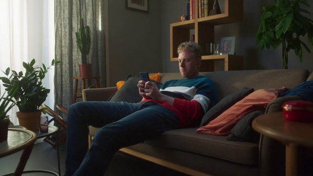 Video Reference: Couch, Living room, Room, Furniture, Home, Sitting, Fun, House, Comfort, Leg, Person, Indoor, Living, Table, Window, Chair, Front, Television, Laptop, Using, Man, Small, Computer, Young, Playing, Video, Screen, Desk, Holding, Woman, Red, Game, Remote, Wall, Clothing, Human face, Sofa bed