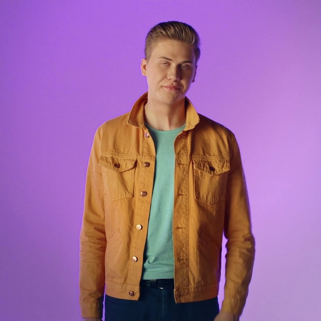 Video Reference: Clothing, Jacket, Purple, Outerwear, Sleeve, Yellow, Leather jacket, Fashion, Leather, Textile, Person, Man, Standing, Wearing, Holding, Front, Posing, Green, Suit, Shirt, Young, Woman, Field, Suitcase, White, Sign, Coat, Human face, Scarf, Hoodie, Collar, Trousers, Hood