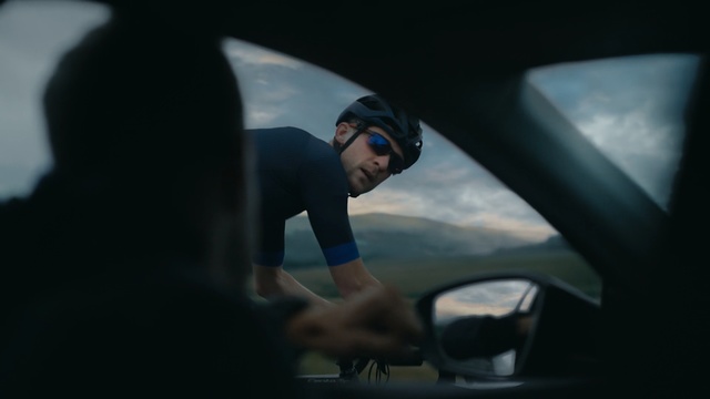 Video Reference: Vehicle door, Windshield, Automotive window part, Automotive mirror, Driving, Rear-view mirror, Automotive design, Auto part, Luxury vehicle, Glass, Person, Outdoor, Man, Object, Thing, View, Car, Mirror, Seen, Riding, Mountain, Head, Woman, Water, White, Holding, Standing, Street, Air, Helmet, Goggles, Human face, Clothing, Personal protective equipment, Image