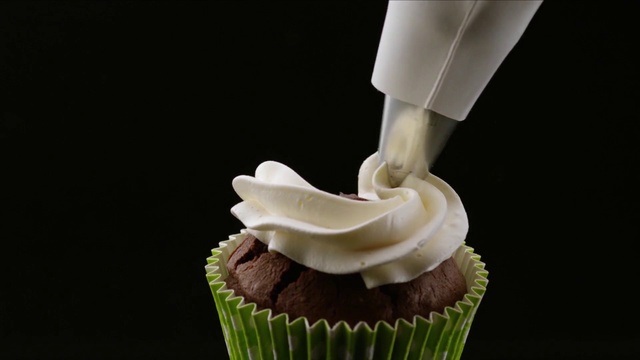 Video Reference: Cupcake, Buttercream, Icing, Food, Cake, Dessert, Cake decorating, Muffin, Cream cheese, Baking cup, Person, Indoor, Cup, Table, Sitting, Decorated, Plate, Small, Chocolate, White, Desert, Green, Cream, Birthday cake, Baked goods, Dairy