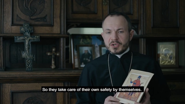 Video Reference: Screenshot, Official, Photo caption, Person, Cabinet, Indoor, Man, Front, Sitting, Holding, Wearing, Table, Kitchen, Black, Laptop, Suit, Glasses, Standing, White, Woman, Young, Computer, Pizza, Human face, Text, Clothing