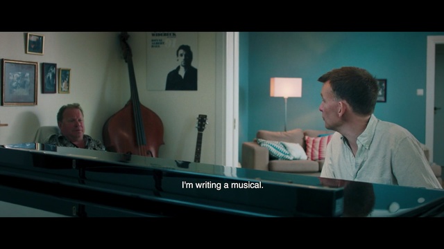 Video Reference: Screenshot, Conversation, Pianist, Sitting, Music, Media, Person, Indoor, Man, Table, Laptop, Computer, Front, Looking, Holding, Room, Screen, Black, Desk, Young, Large, Bed, Video, Blue, Wall, Piano, Text, Musical instrument