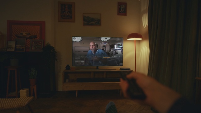 Video Reference: Room, Property, Sky, House, Television, Technology, Floor, Hardwood, Electronic device, Flooring, Indoor, Living, Cat, Front, Sitting, Screen, Looking, Man, Flat, Watching, Small, Table, Standing, Monitor, Laying, Holding, Playing, White, Video, Computer, Wall, Furniture, Person, Human face, Desk, Computer monitor