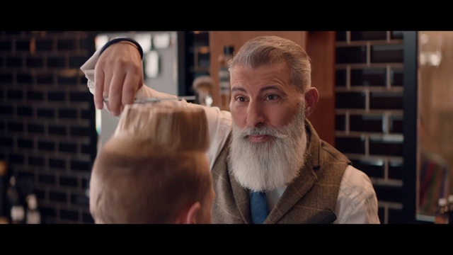 Video Reference: Facial hair, Beard, Moustache, Human, Photo caption, Screenshot, Person, Man, Indoor, Standing, Suit, Front, Looking, Wearing, Table, Holding, Orange, Mouth, Food, Human face, Human beard, Clothing, Face