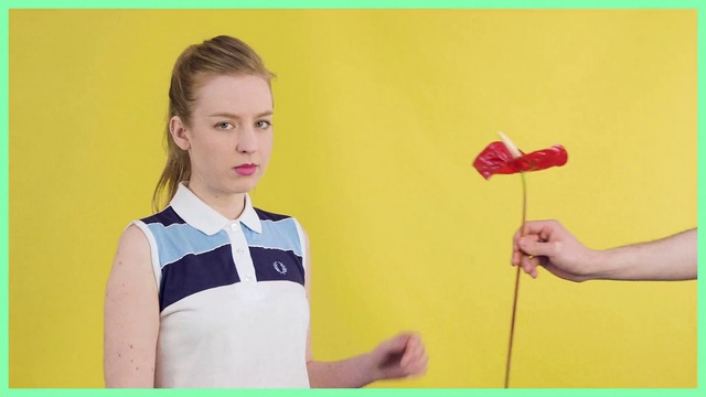 Video Reference: Yellow, Arm, Neck, Finger, Plant, Flower, T-shirt, Gesture, Person, Indoor, Boy, Young, Standing, Holding, Man, Small, Umbrella, Child, Posing, Front, Wearing, Remote, Playing, Table, White, Video, Sign, Wii, Game, Television, Room, Shirt, Board, Woman, Wall, Text, Human face, Clothing, Accessory