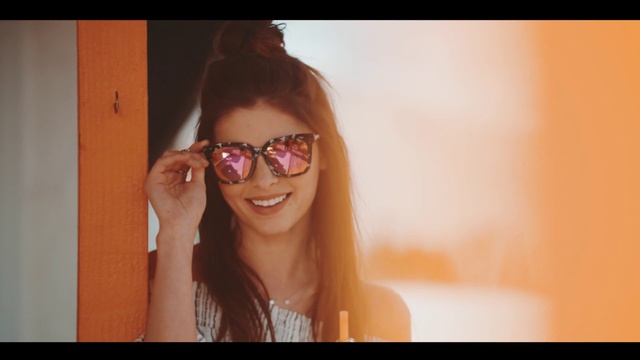 Video Reference: Eyewear, Face, Hair, Glasses, Sunglasses, Lip, Facial expression, Cool, Skin, Eyebrow, Person, Clothing, Orange, Looking, Woman, Man, Holding, Cellphone, Phone, Front, Wearing, Smiling, Sitting, Shirt, White, Young, Black, Standing, Room, Red, Human face, Wall, Smile, Goggles, Girl, Fashion accessory, Spectacles