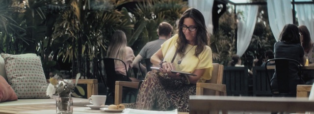 Video Reference: Eyewear, Long hair, Fur, Brown hair, Art, Person, Table, Woman, Sitting, Outdoor, Bench, Front, Food, Girl, People, Young, Eating, Man, Park, Laptop, Cake, Wooden, Restaurant, Group, Plate, White, Clothing, Human face, Glasses, Smile